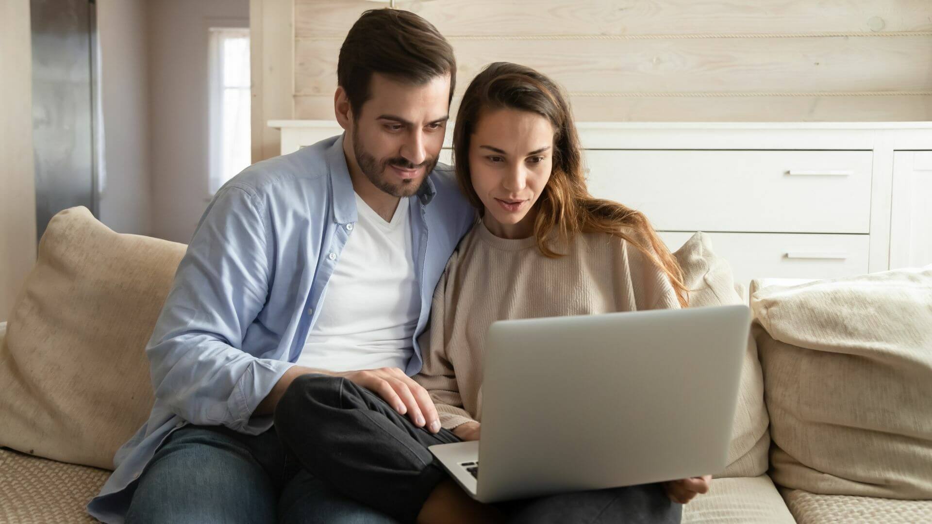 Couple sitting together at home researching Michigan land for sale on a laptop during winter
